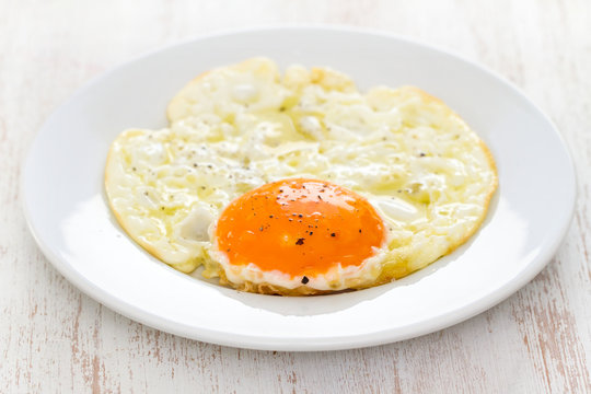 fried egg on white plate on wooden background