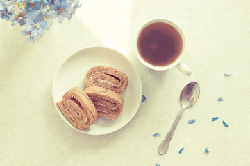 Delicious breakfast - biscuit roll with tea on a background of sunny violets