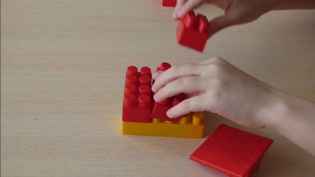 Kid create small house from plastic bricks. Educational game - construction of toy building.