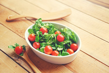 Cherry tomatoes and basil salad in a white cup on a wooden table.