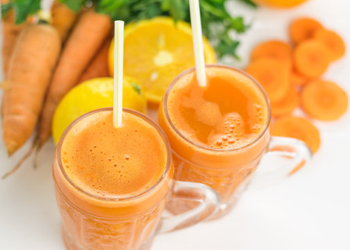 Two glass mugs with a carrot smoothie on a white wooden table.