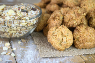 Homemade cookies on a piece of burlap and a bowl of muesli on a wooden table.