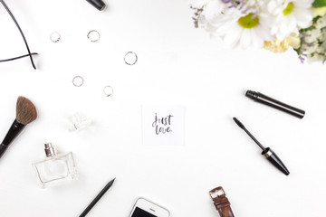 A bouquet of flowers with Just love written in calligraphic style on paper on flowers on a white background with female things. Flat lay, top view