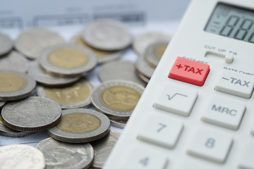 Close up macro shot of calculator with tax button in red with pile of coins as background. Income, tax, financial data.