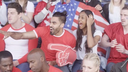 Crowd of spectators watching sports game in stadium waving to camera