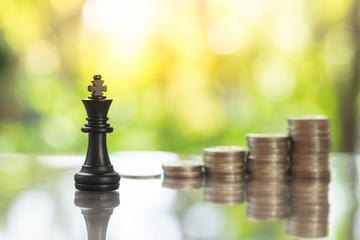 Chess pieces with coins stacks as backdrop, business strategy, decision making.