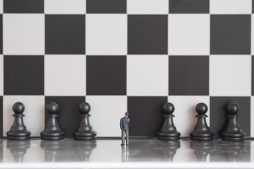 Business decision making concept. Miniature people : small businessman figure standing against chessboard wall with chess pieces