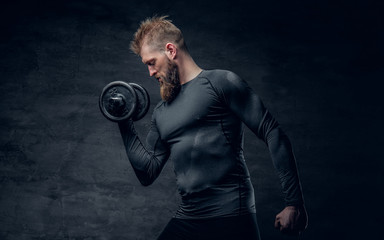 Sporty bearded male in a grey sportswear holds dumbbell.