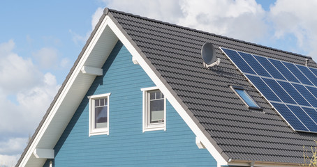 blaues Haus mit Solarzellen und Fenstern im Giebel