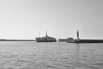 Black and white photography of traditional public ferry arriving to Kadikoy station. Water breaker and a motorboat are also in the view.