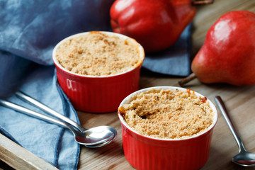 Close-up of a portion desserts pear crumble pie in a red bowls on a wooden table.