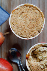  Top view of a portion dessert pear crumble pie in a red bowl on a wooden table. 
