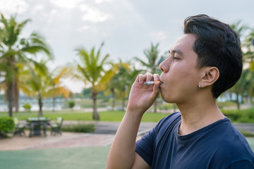 casual young man and smoking a cigarette in his mouth.
Man smoking a cigarette on park outdoor.