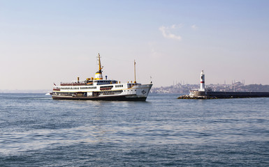 Traditional public ferry arriving to Kadikoy station in Istanbul. Water breaker is also in the view. Hagia Sophia and Blue Mosque are in the background.