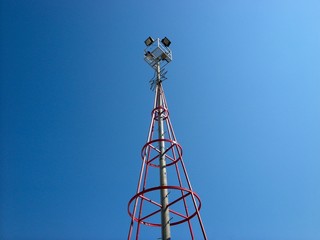 Stahlkonstruktion eines roten Lichtmast mit Scheinwerfer vor blauem Himmel im Sonnenschein in der...