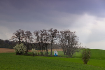Santa Barbara chapel landscape at spring, South Moravia, Czech Republic. Chapel in a field surrounded by trees with dramatic cloudy skies. Sun rays illuminate the chapel through clouds.