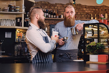 Two bearded hipster coffee shop owners at the counter.