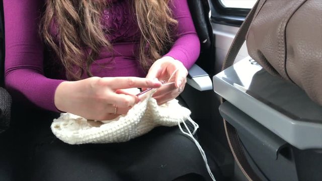 The girl is engaged in knitting in a train. Sits at the window of a train. On the knees lies a tangle of thread. Video shot on the iPhone 7 Plus.