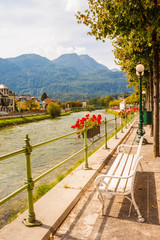 Vacant white bench on riverside esplanade facing river Traun and mountains on a sunny summer day in a resort town Bad Ischl, Austria.