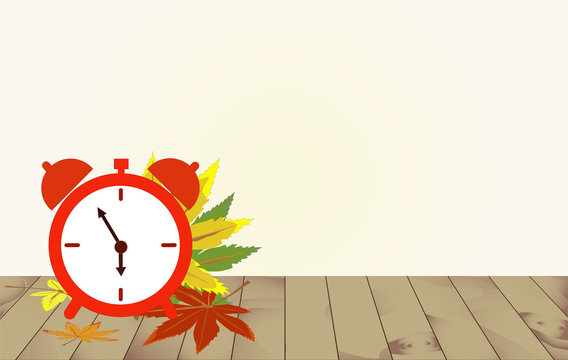 Red alarm clock and maple leaves on a wooden table.