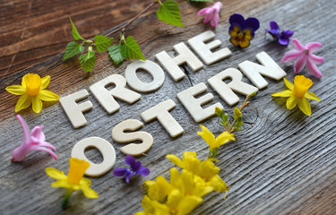 Frohe Ostern auf Holzhintergrund mit Osterglocken und bunten Blumen dekoriert