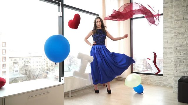 Cinemagraph beautiful brunette woman standing in long dress on the background of large Windows.