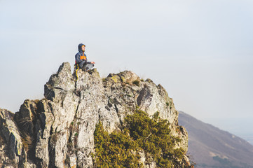 The young climber meditates in the lotus position on top of a steep cliff against the backdrop of the city and mountains