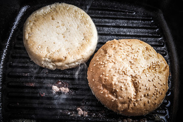 Sesame buns in a frying pan grill. Preparing ingredients for hamburger. Selective focus. Shallow depth of field. Toned