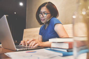Happiness of Asian glasses Woman using cell phone and laptop. Graph financial diagram documents and...