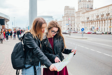 Fototapeta premium Two young stylish women traveling and looking at the map in city