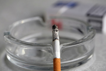 Cigarette on glass ashtray; health, industry and addiction concept.