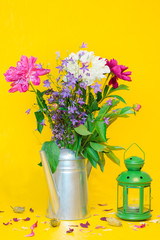 A still life with a beautiful white and purple peonies bouquet and a green lantern on the blurred yellow background
