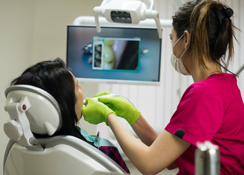 Dentist at work examining woman's teeth in dental clinic with remote camera. Picture of teeth is on the screen. New dental technologies.