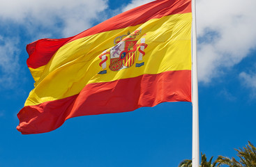 Spanish flag against the blue sky. Sunny weather. It's windy. White clouds against blue sky.
