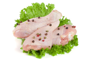 Three raw chicken drumsticks on lettuce leaf with peppercorns isolated on white background