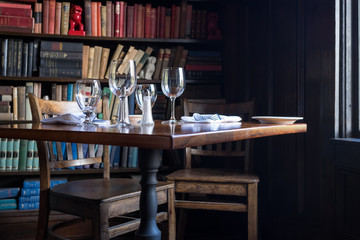 Table set for two with wine glasses by window with books in the background. Intimate, private, cozy feeling.