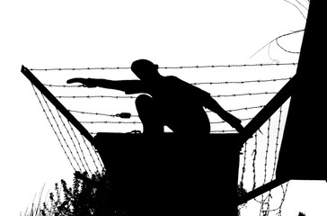 Silhouette von einem flüchtenden Mann über Stacheldraht