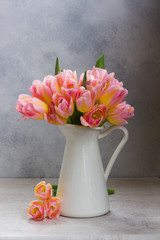 Bunch of pink and yellow tulips in white vase on gray background