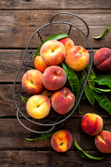 Naklejka na ściany i meble Fresh peaches fruits with leaves in basket on dark wooden rustic background, top view