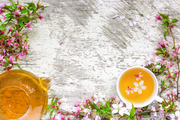 cup of green tea and teapot with branches of blossoming sakura and cherry