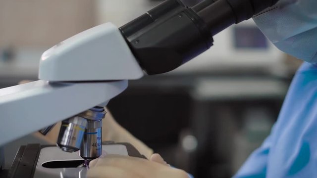Crop shot of laboratory worker using microscope. Crop faceless shot of female specialist in uniform using microscope.