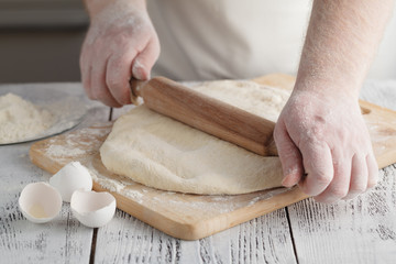 male cook rolling out dough on the table, closeup shot