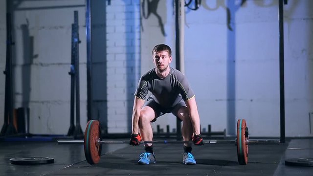 Strong man doing an exercise with a barbell in the gym on a background of a gray concrete wall