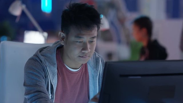  Close up portrait young Asian computer game designer working at his desk