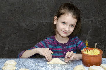 Fototapeta na wymiar Little girl sculpts potato pies. The gray background.