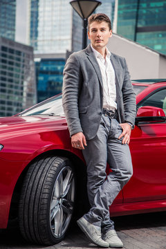 стильный мужчина в костюме стоит возле своего дорогого авто