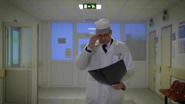 Mature male doctor with radiogram. Male doctor in uniform walking in hospital with radiogram and investigating it.