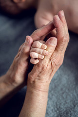 great-grandmother holds the hands of his beloved grandson by the window