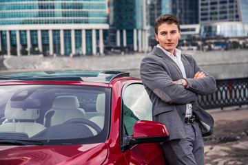стильный мужчина в костюме стоит возле своего дорогого авто