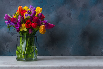bunch of bright spring flowers in vase on dark background with copy space
